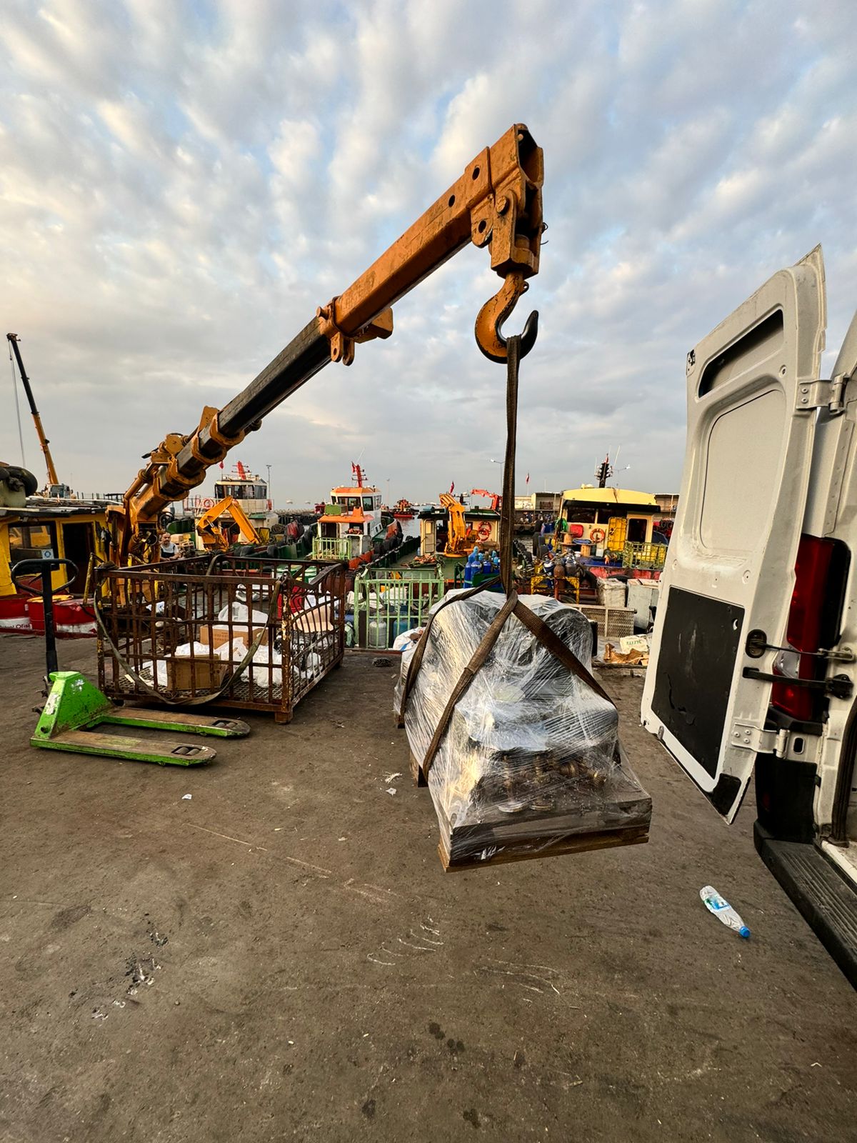 Crane loading wrapped marine equipment beside a delivery vehicle at the port